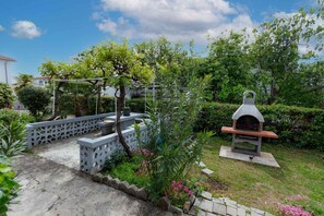 Een tuin met een barbecueplek, een pergola en een witte hekken.