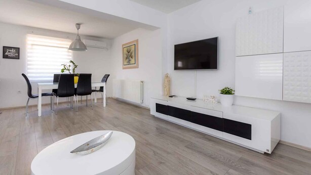 Un salon moderne comprenant un coin repas, des meubles blancs, un téléviseur à écran plat et un radiateur.