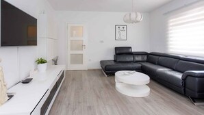 Un salon moderne avec un canapé en cuir noir, une table basse blanche, un téléviseur à écran plat fixé au mur et une décoration minimaliste.