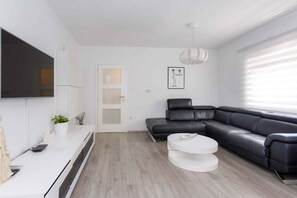 Een moderne woonkamer met een zwarte leren bank, een witte salontafel, een flatscreen televisie aan de muur en een minimalistische inrichting.