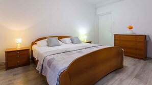 Une chambre à coucher avec un lit en bois, deux tables de chevet avec des lampes, une commode et une porte.