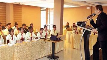 A conference room with a speaker at a podium and attendees seated at a long table.