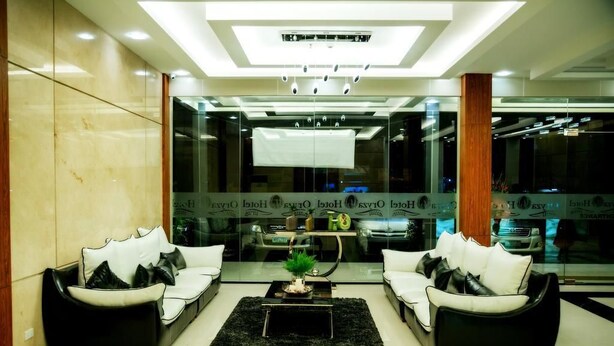 Een moderne lobby met twee zwarte leren banken, een zwart tapijt en een glazen wand met reflecties.