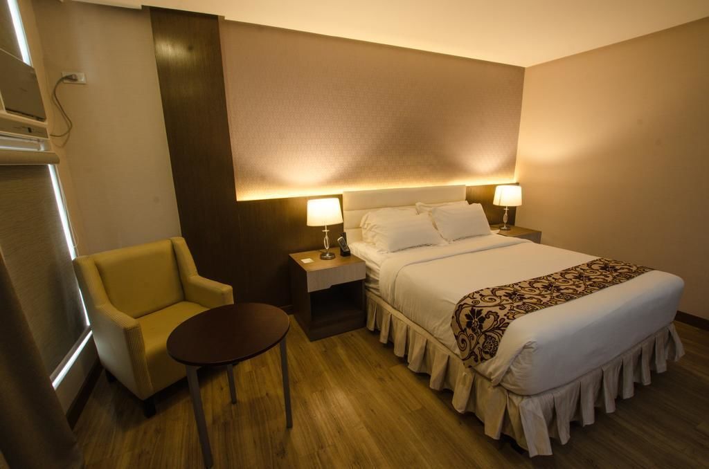 A hotel room with a bed, bedside lamps, a small table, a chair, and a wall-mounted TV.