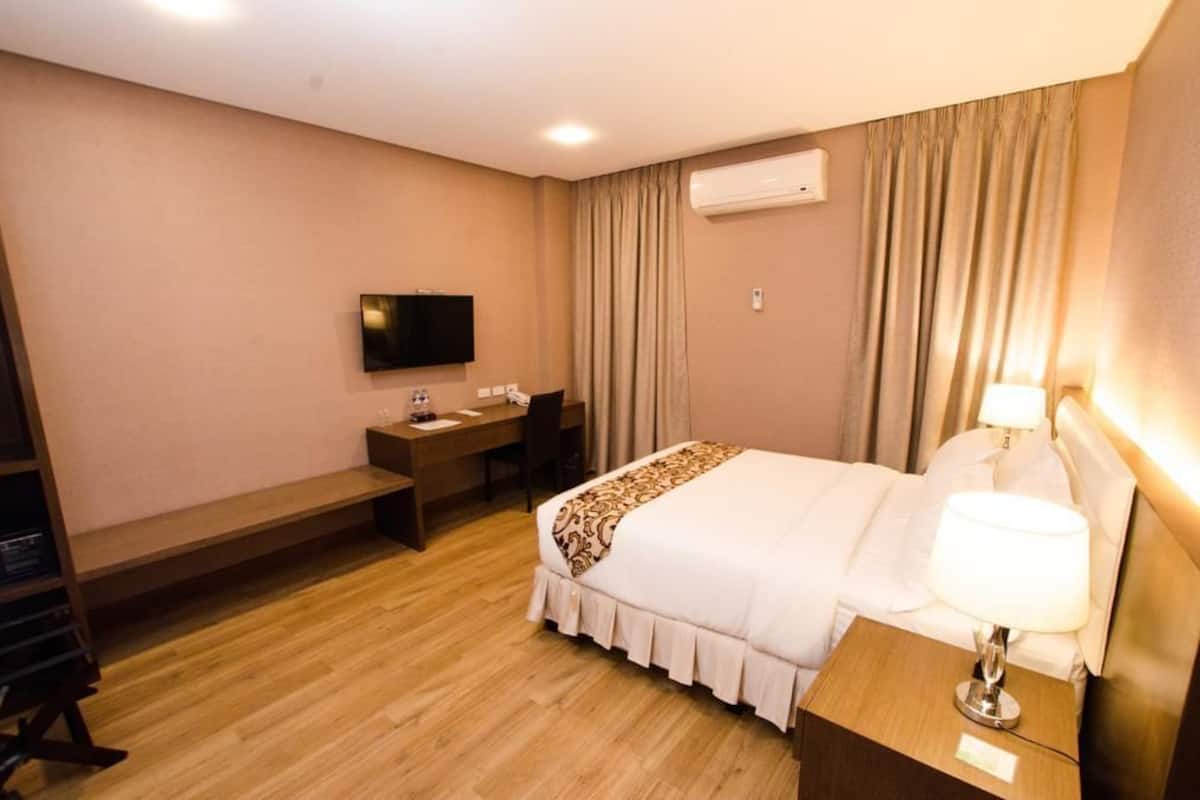 A hotel room with a bed, bedside table, desk, chair, and a flat-screen TV mounted on the wall.