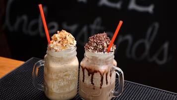 Two iced coffee drinks in mason jars with orange straws, placed on a black textured mat.