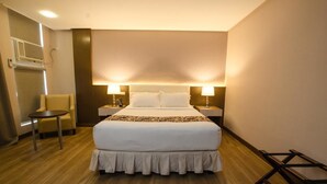 Een hotelkamer met een groot bed, twee bedlampen, een klein rond tafeltje, een stoel en een houten vloer.
