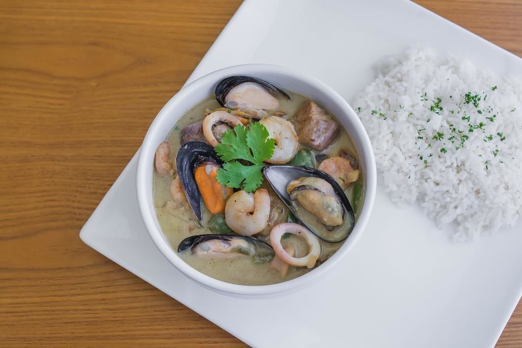 Eine Schale mit Fisch- und Meeresfrüchtestew und Reis auf einem weißen Teller.