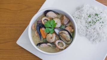 Eine Schale mit Fisch- und Meeresfrüchtestew und Reis auf einem weißen Teller.