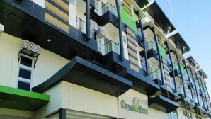 Een meerlaags hotel met balkons, een groen luifel en een bord waarop 'Oryza Hotel' staat.