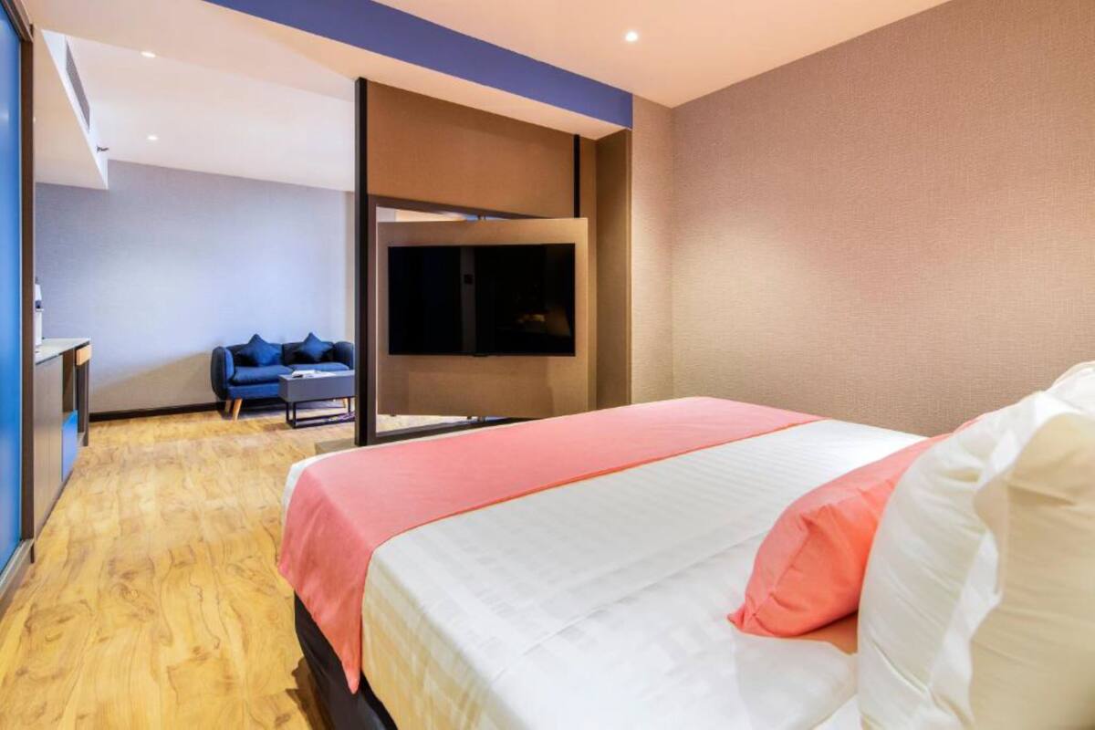 A modern hotel room with a large bed, a TV mounted on the wall, and a seating area with a blue sofa.