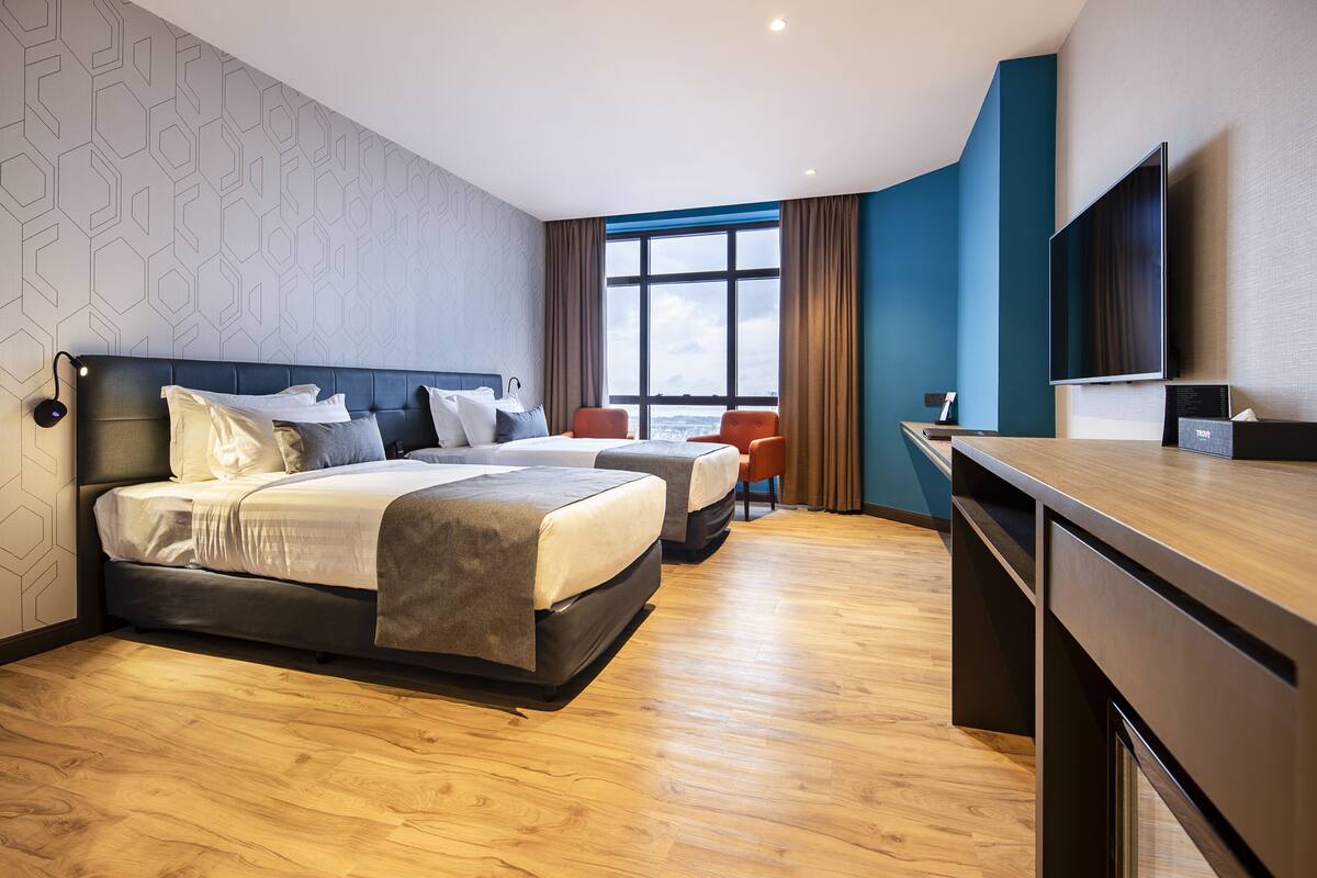 A hotel room with two beds, a desk, and a large window with a view.