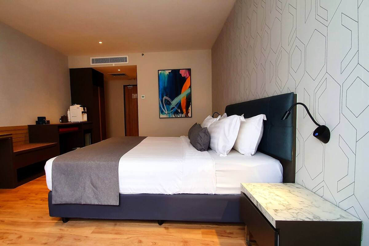 A hotel room with a bed, bedside table, desk, and a flat-screen TV mounted on the wall.