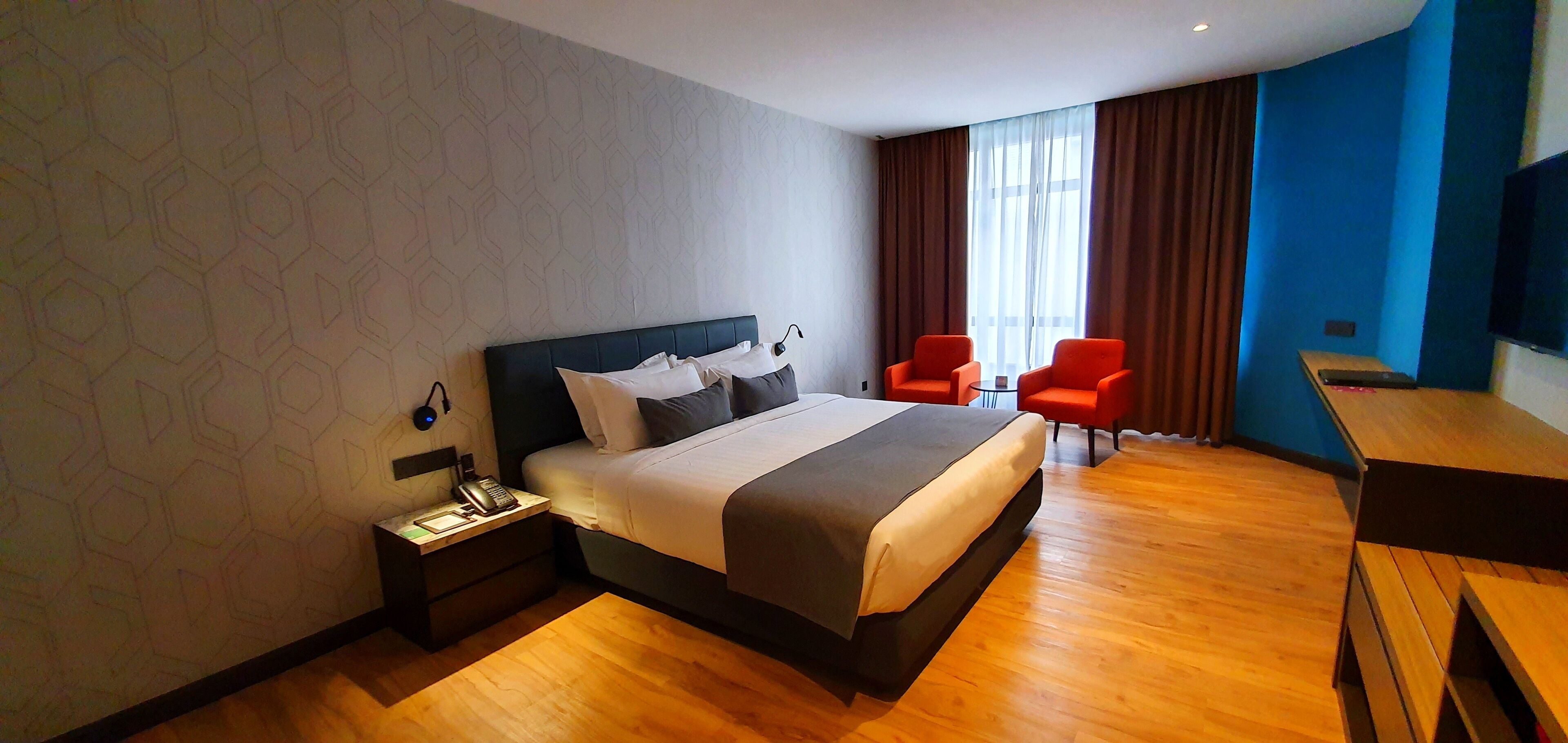 Habitación de hotel con una cama grande, un escritorio con silla y televisor montado en la pared.
