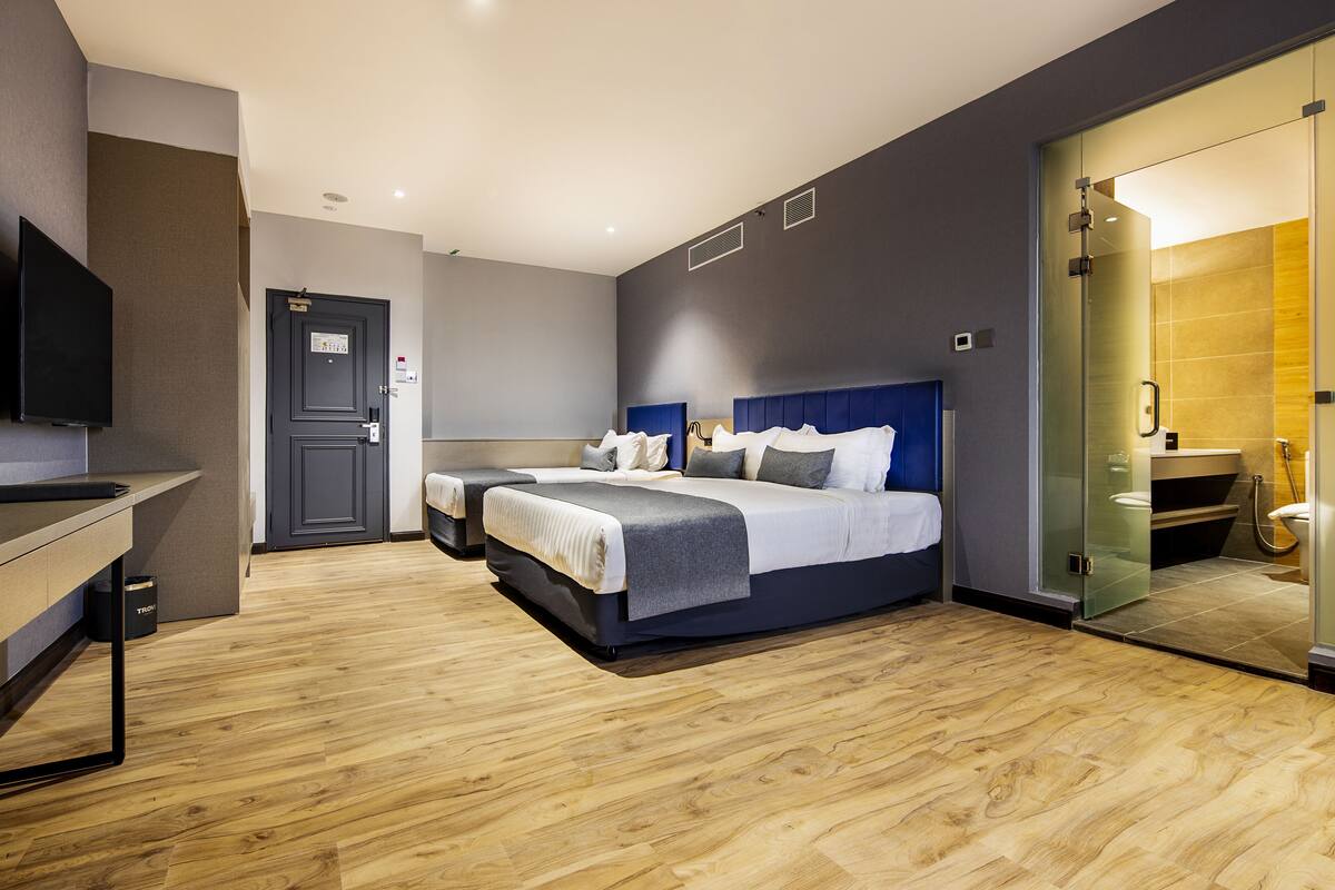 A modern hotel room with a large bed, a bedside table, a TV, and a glass shower enclosure.