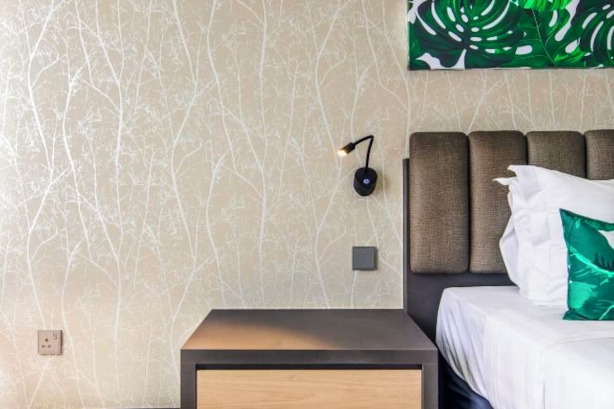 A hotel room with a bed, a nightstand, a wall-mounted lamp, and a large abstract painting.