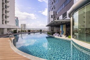 A rooftop swimming pool with a wooden deck, lounge chairs, and a glass-enclosed area with seating. - TROVE Johor  Bahru (Johor Bahru)