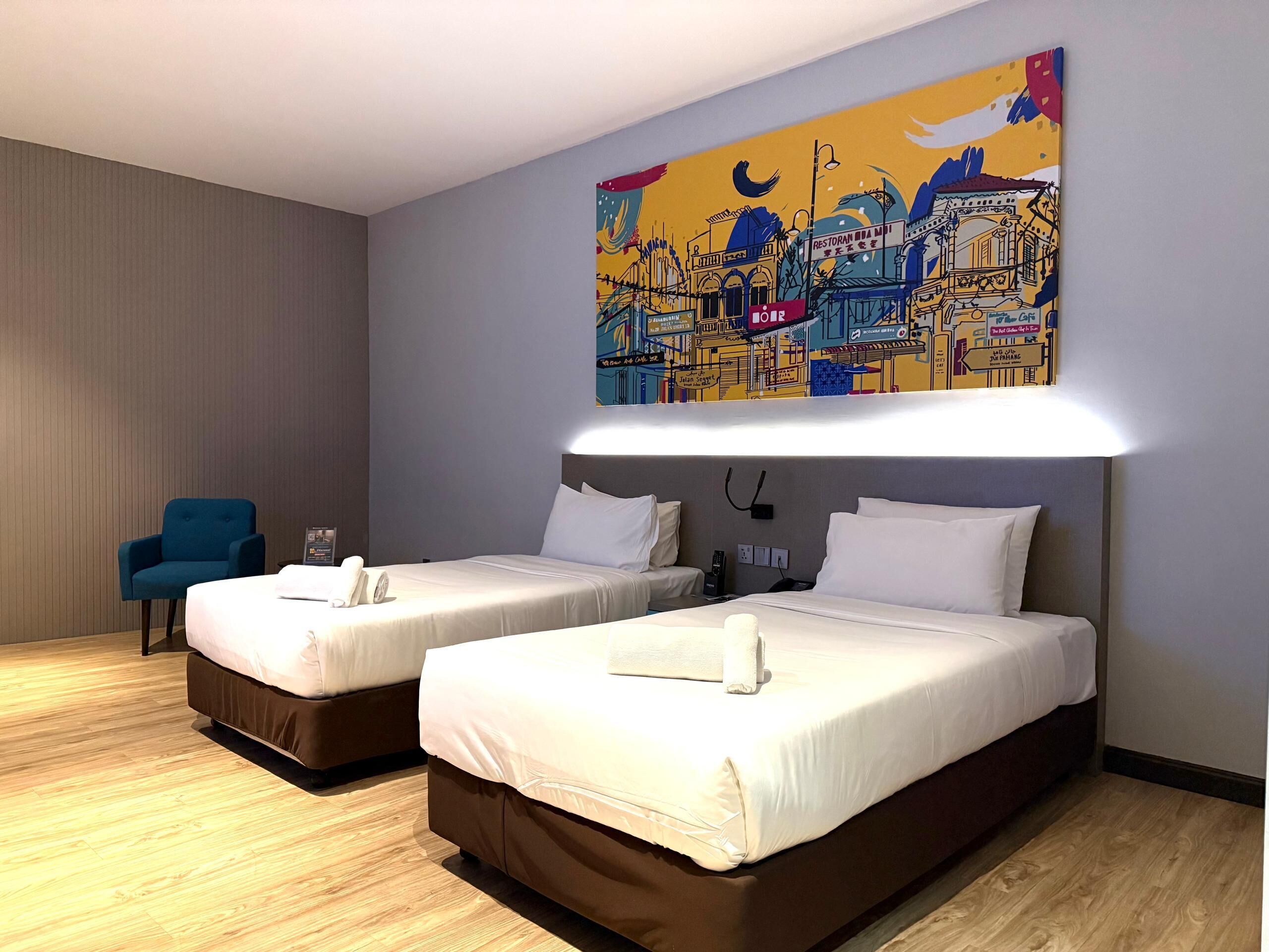Habitació d'hotel amb dos llits, un butàc blau i un mural colorit a la paret.