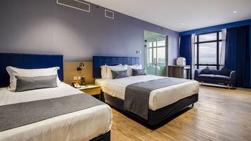 A hotel room with two beds, a sofa, a desk, and a large window with curtains.