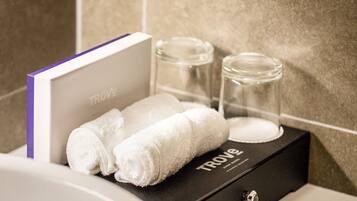 A bathroom with a white sink, a towel, a glass jar, and a book titled "TROVE" on a black box.