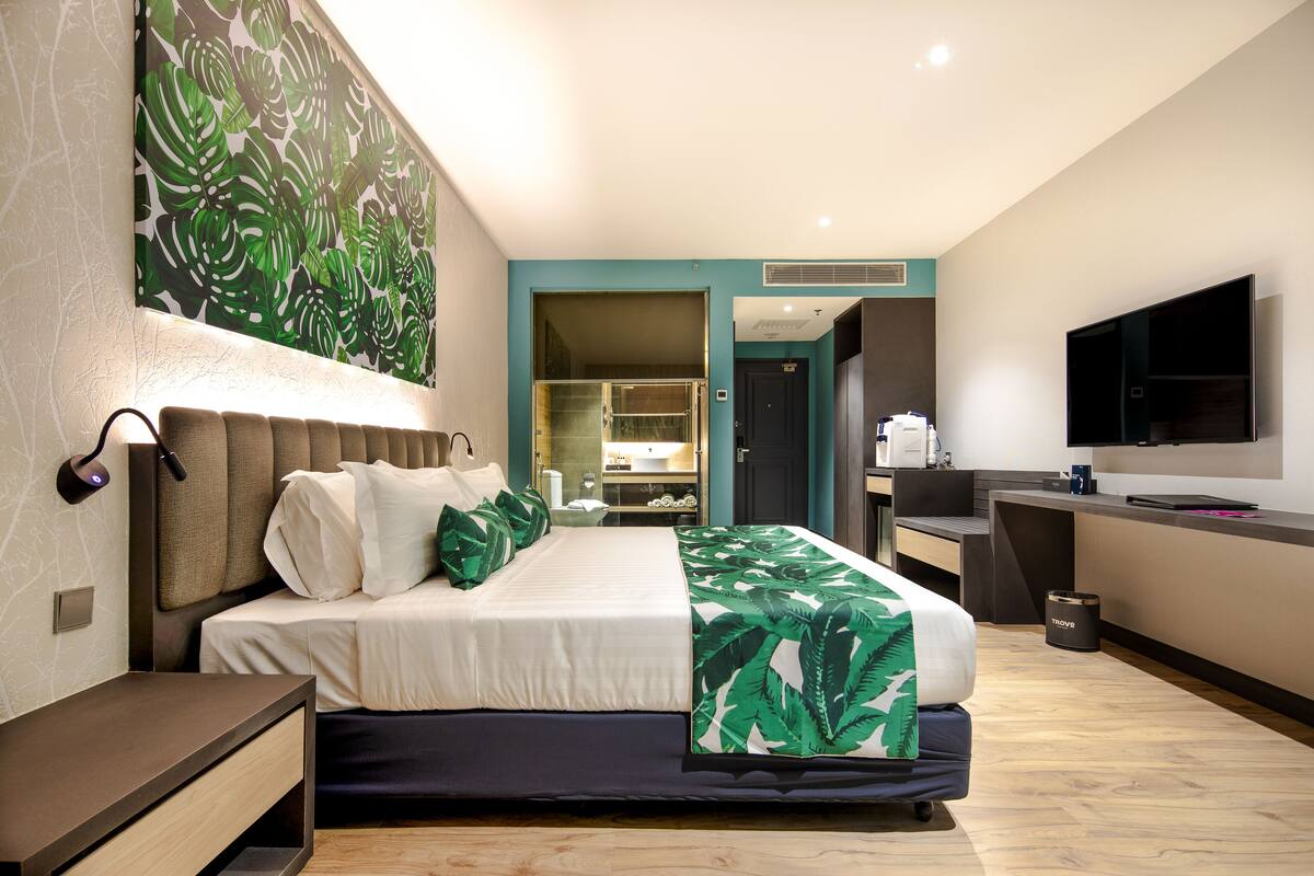 A modern hotel room with a large bed, a desk, a flat-screen TV, and a bathroom visible through an open door.