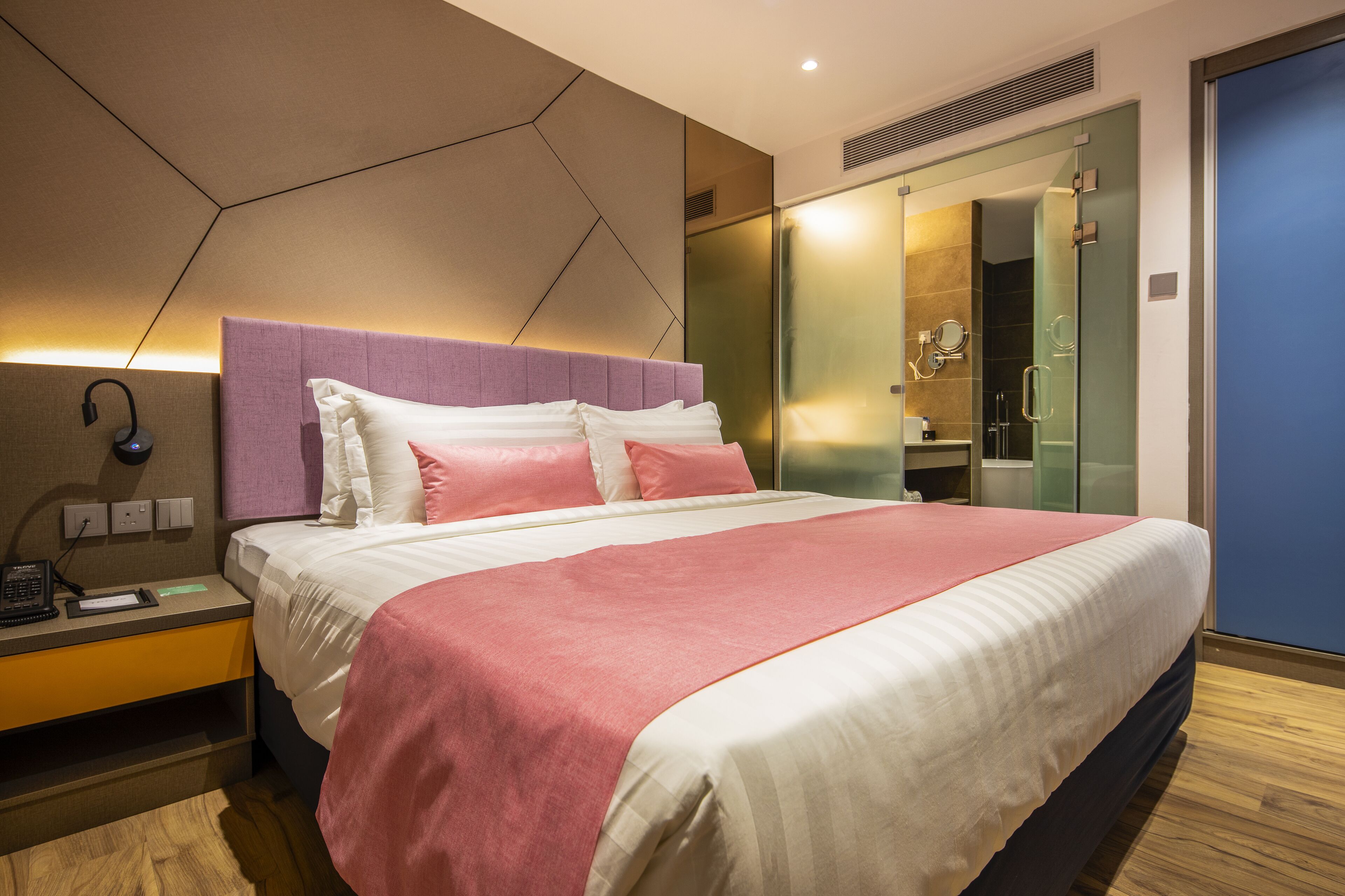 A modern hotel room with a large bed, a bedside table, a mirror, and a wardrobe.