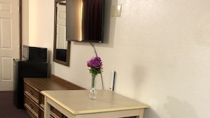 A hotel room with a wooden desk, a chair, a television mounted on the wall, and a vase with flowers on the desk. - Rexdale Inn (Seminole)