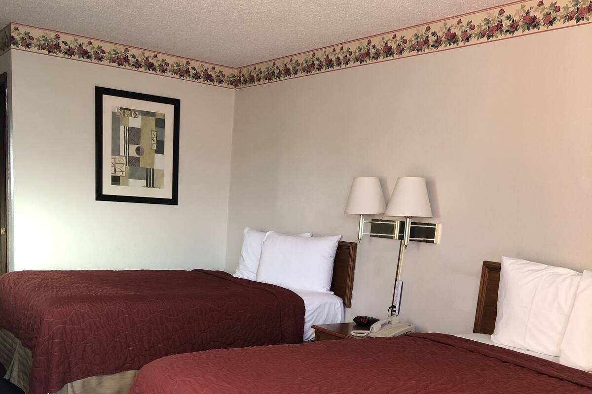 A hotel room with two beds, a nightstand, a lamp, and a framed picture on the wall.