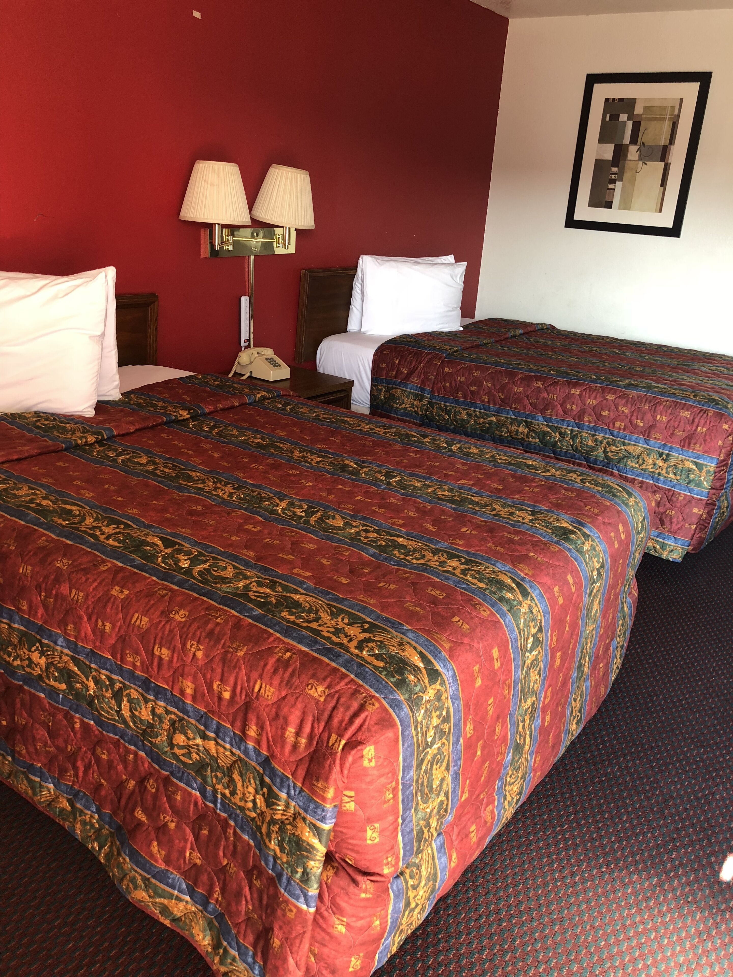 Una habitación de hotel con dos camas, un teléfono, dos lámparas y un cuadro en la pared.