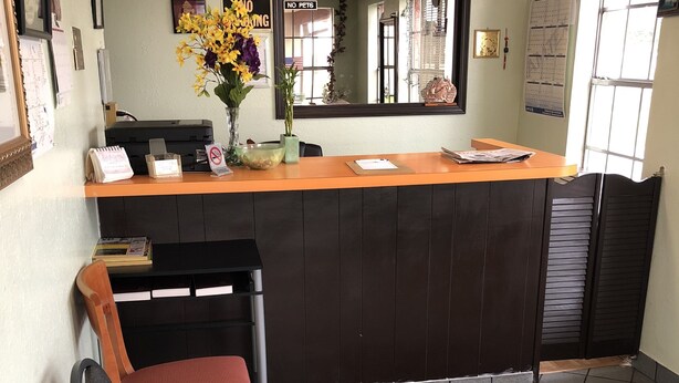 A reception area with a counter, chairs, a desk, a vase with flowers, and a 'No Pets' sign. - Rexdale Inn (Seminole)