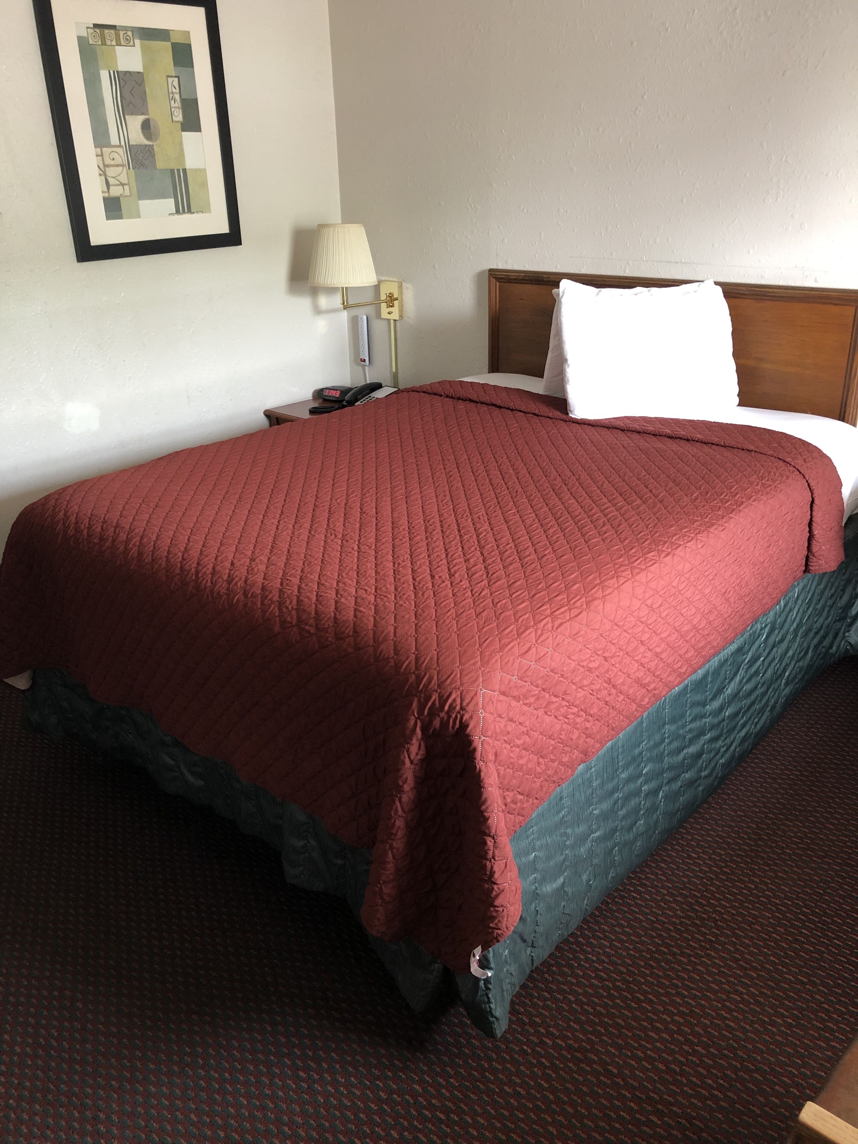 Una habitación de hotel con una cama grande, una mesita de noche, una lámpara y un cuadro en la pared.