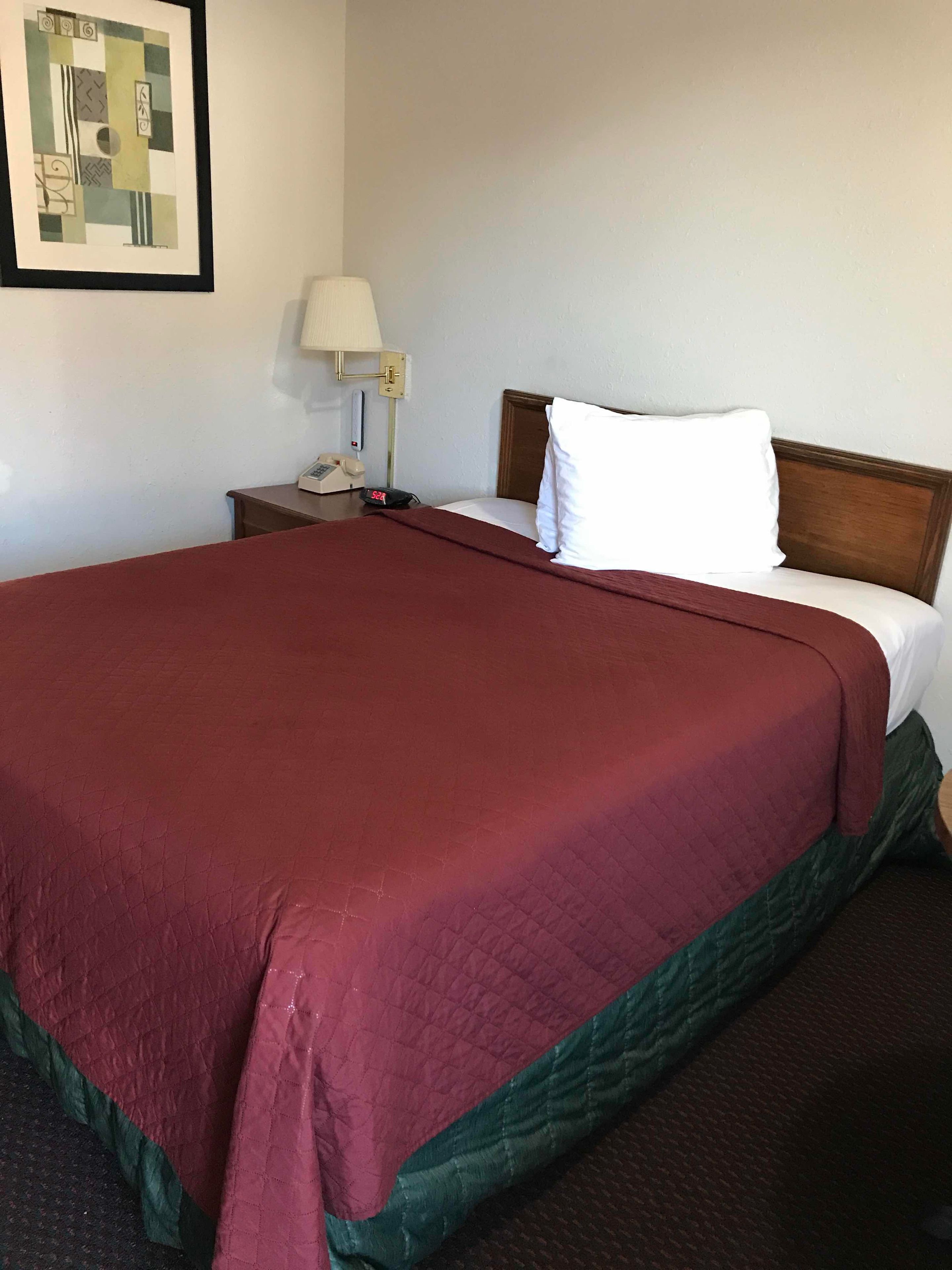 A hotel room with a large bed, a nightstand with a lamp, and a telephone.