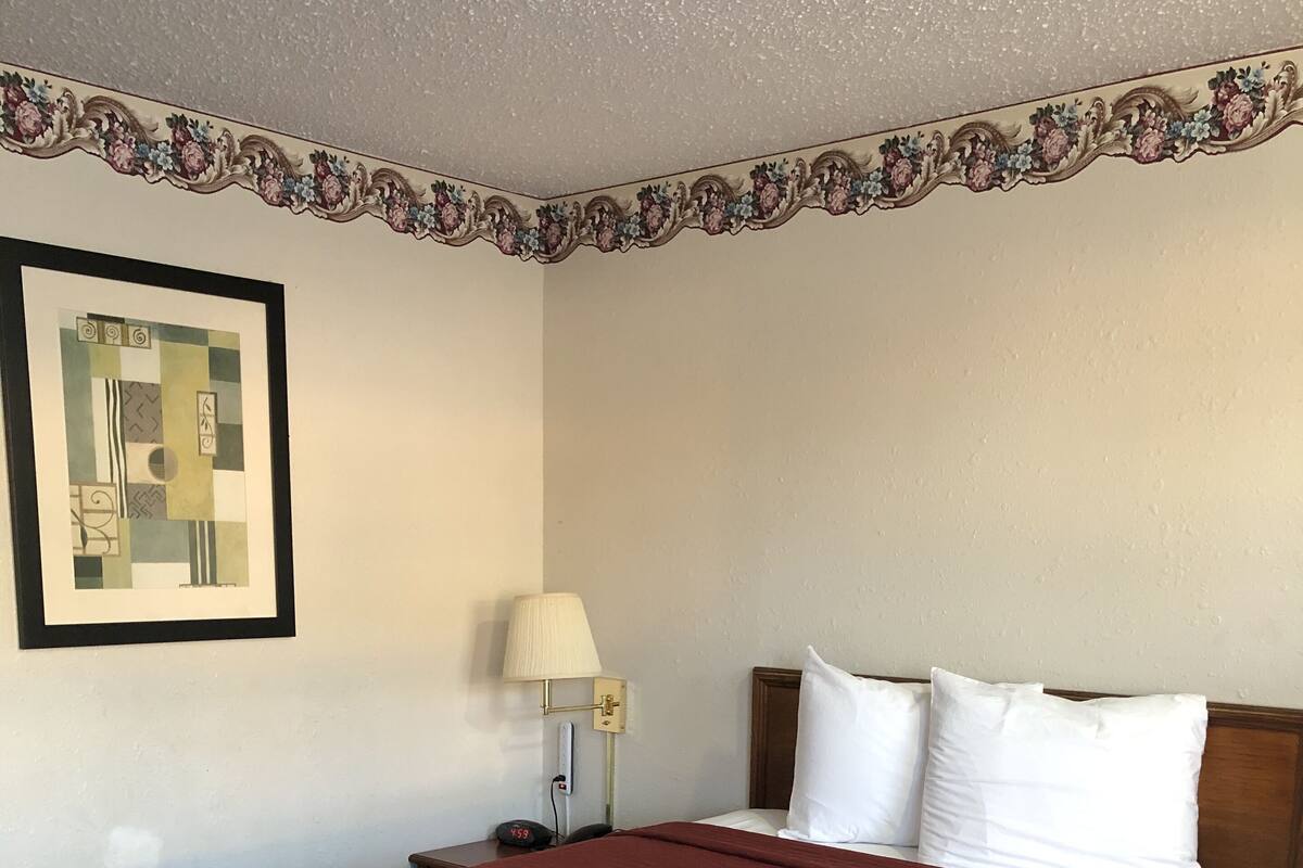 A hotel room with a large bed, a nightstand with a lamp, a framed picture on the wall, and a decorative border.