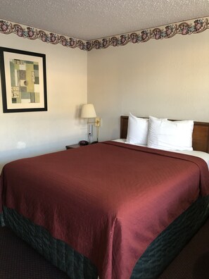 A hotel room with a large bed, a nightstand with a lamp, a framed picture on the wall, and a decorative border. - Rexdale Inn (Seminole)