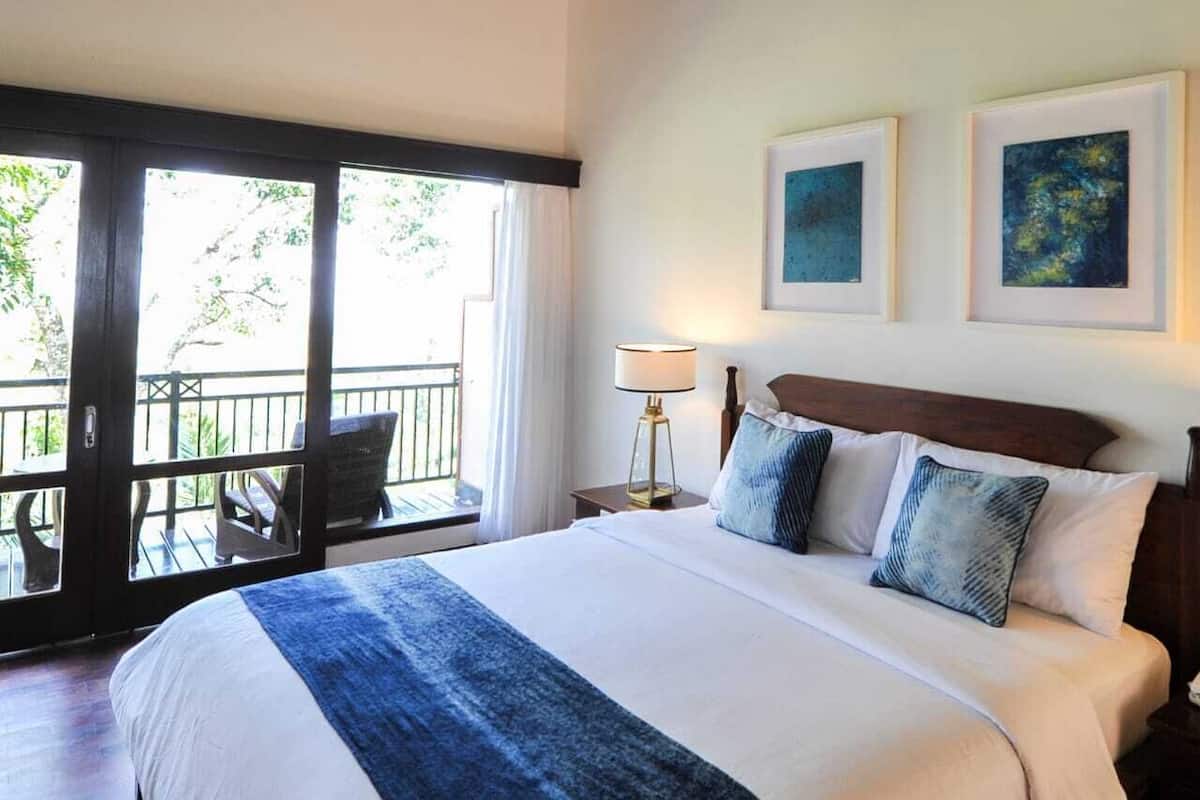 A hotel room with a large bed, a balcony with chairs, and two framed artworks on the wall.