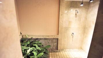 A small, tiled shower area with a stone wall and a potted plant.
