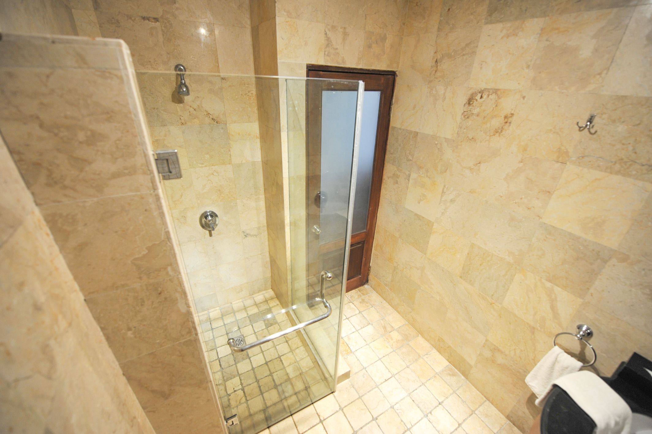 Un baño con cabina de ducha de vidrio, suelo de baldosas y puerta de madera.