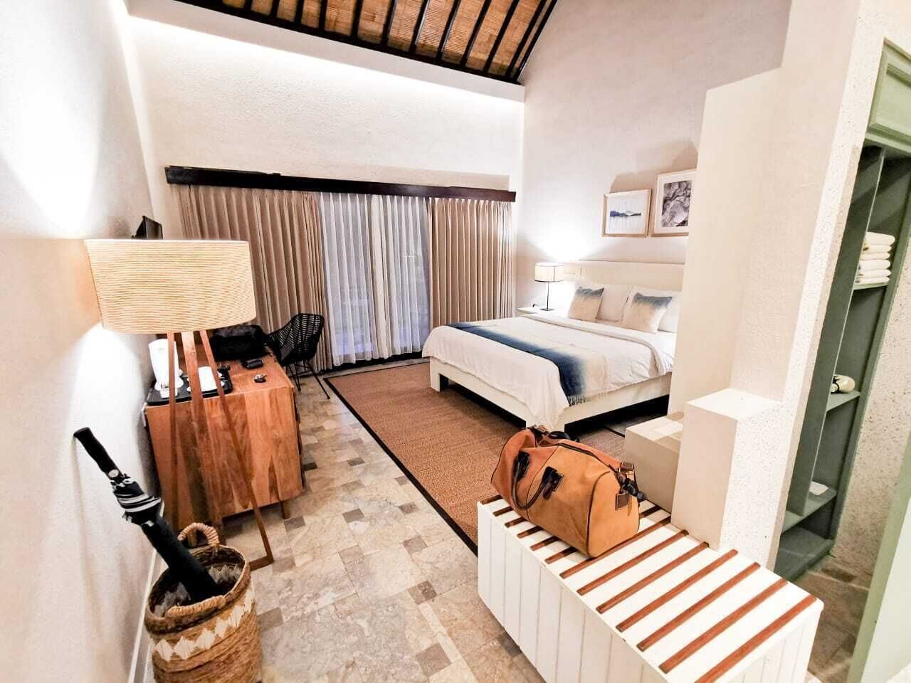 A hotel room with a bed, a desk, a chair, a lamp, and a suitcase.