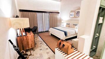A hotel room with a bed, a desk, a chair, a lamp, and a suitcase.