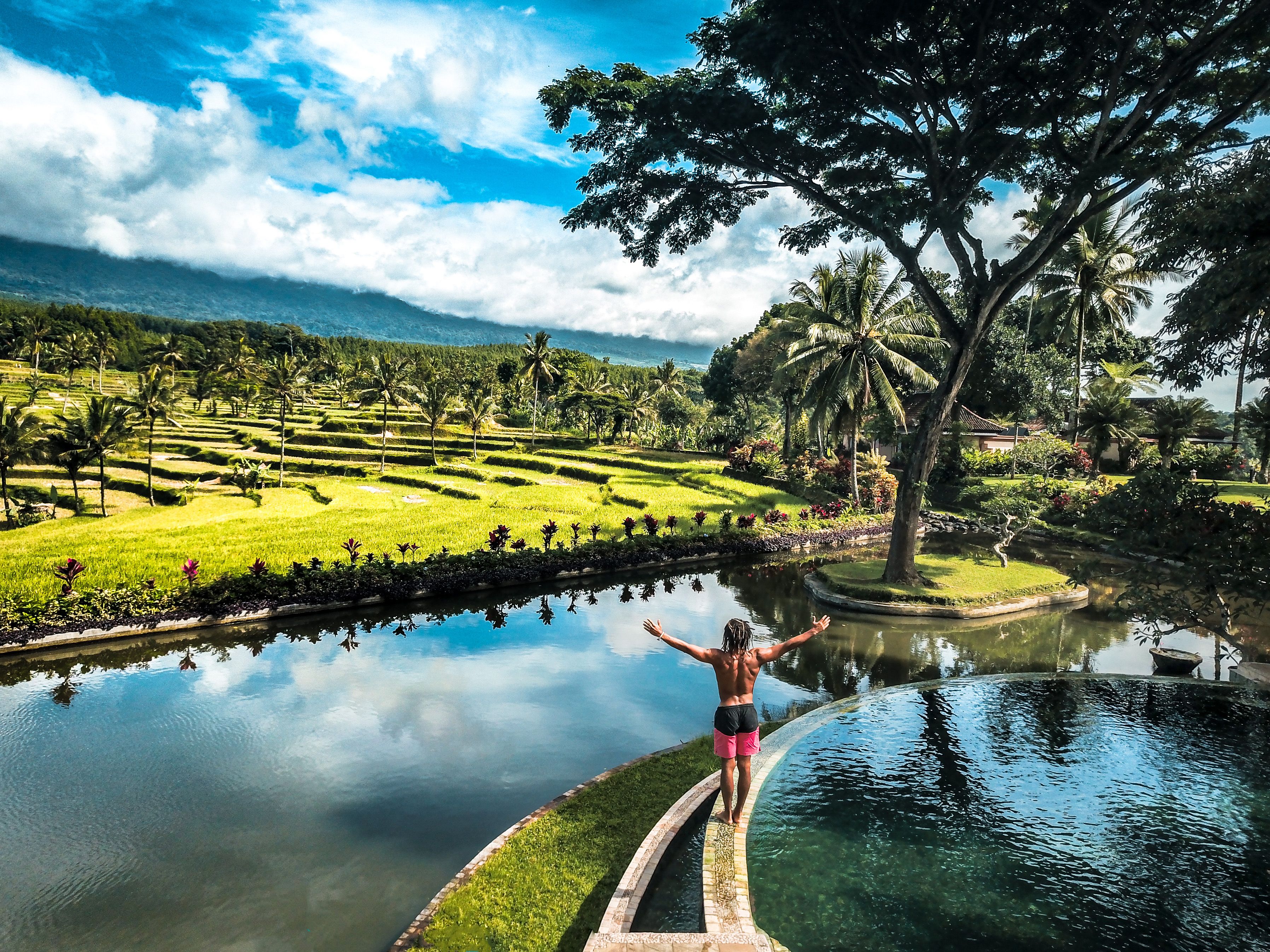 Un hombre está de pie junto a la piscina, con vistas a un paisaje exuberante y palmeras.