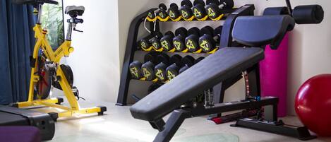 A gym with exercise equipment, including a bench, dumbbells, and a stationary bike.