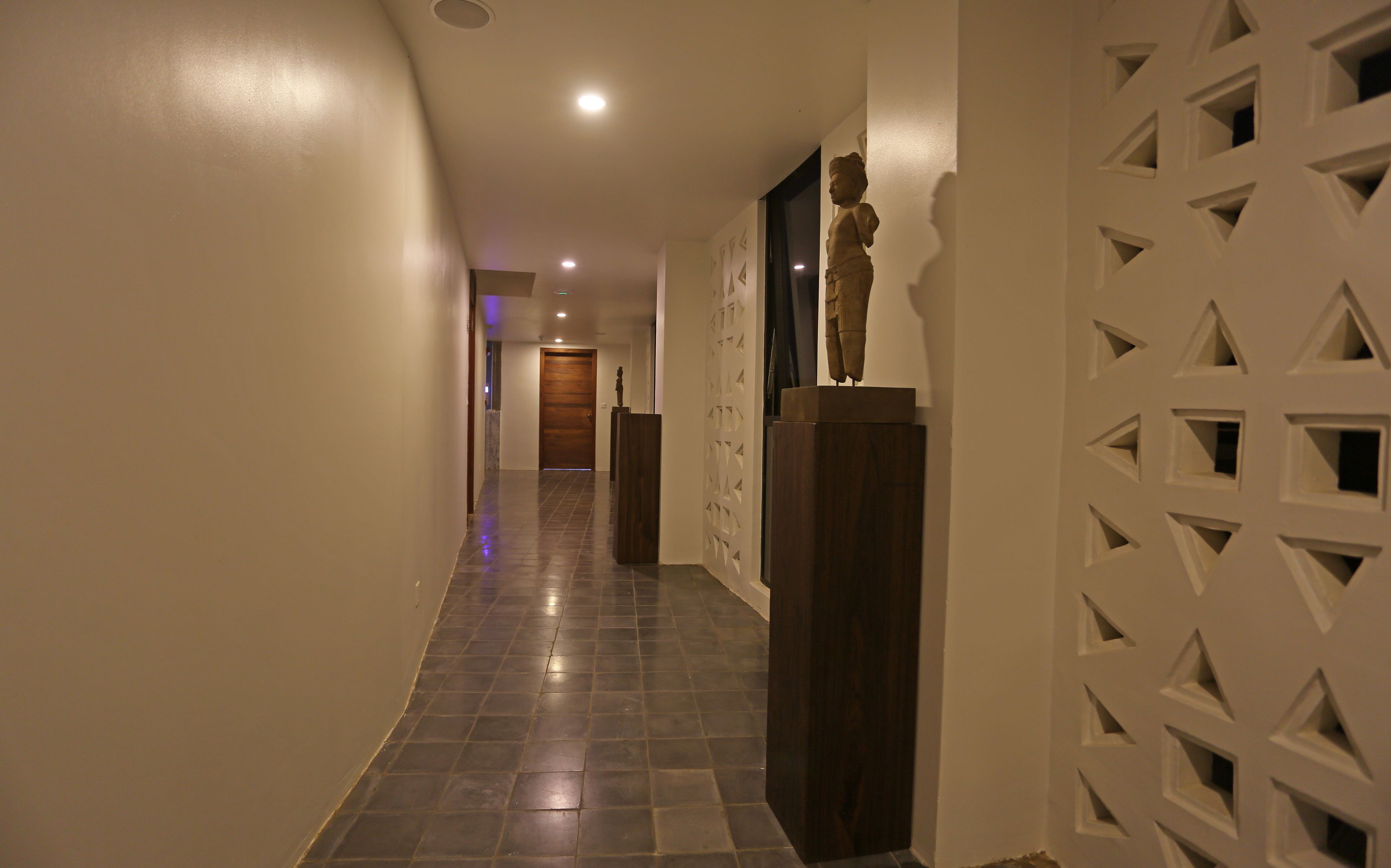 A hallway with a tiled floor, a wooden door at the end, and a decorative wall with geometric patterns.