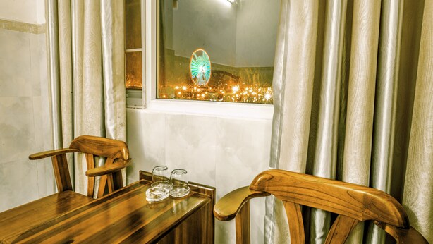 A dining area with a wooden table and chairs, a window with curtains, and a view of a Ferris wheel. - Lucky Star hotel (Da Nang)