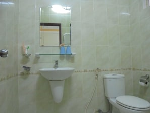 Un baño con lavamanos blanco, un espejo, un inodoro y un estante de vidrio con artículos de aseo.