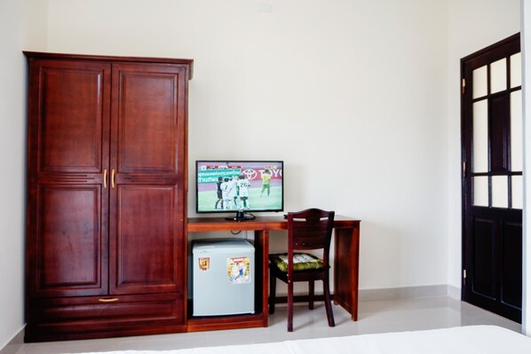 A room with a wooden wardrobe, a small refrigerator, a television on a desk, and a chair. - Lucky Star hotel (Da Nang)