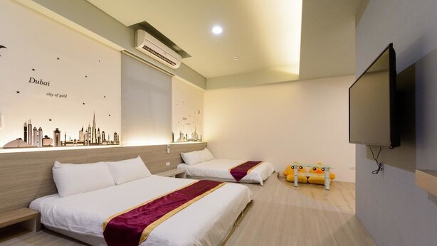 A hotel room with two beds, a flat-screen TV, and a wall mural of Dubai skyline. - ANKES Hostel (Hengchun)