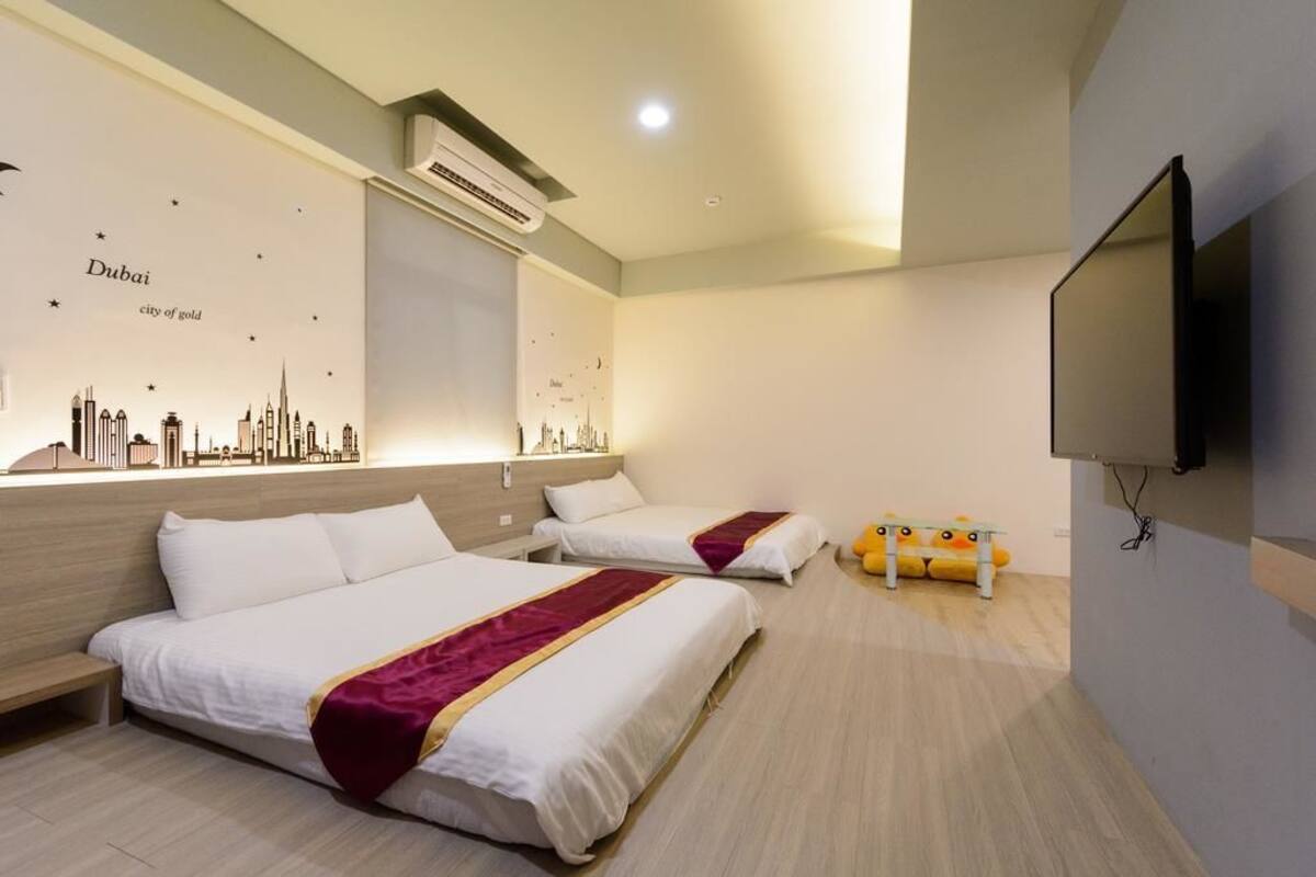 Habitación de hotel con dos camas, un televisor de pantalla plana y un mural en la pared con el horizonte de Dubái.
