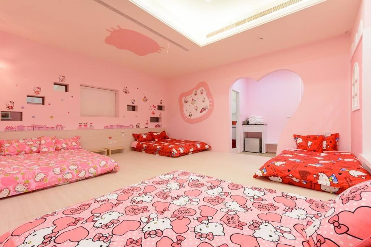 Un dormitorio con temática rosa, con tres camas, cada una con colcha de Hello Kitty, y un ventanal grande.