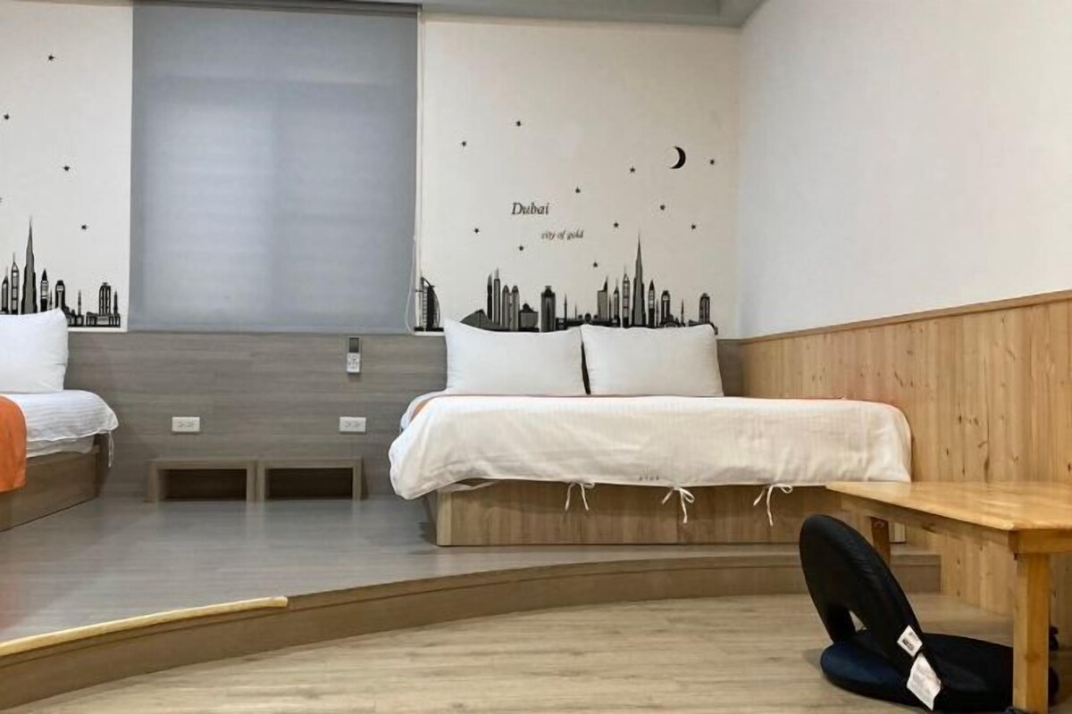 Una camera d'albergo con due letti, una panca in legno e un murale raffigurante una veduta urbana.