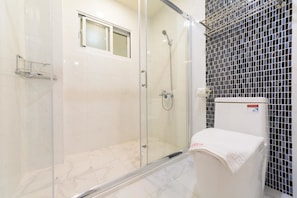 A glass-enclosed shower area with a white toilet and a tiled wall. - ANKES Hostel (Hengchun)